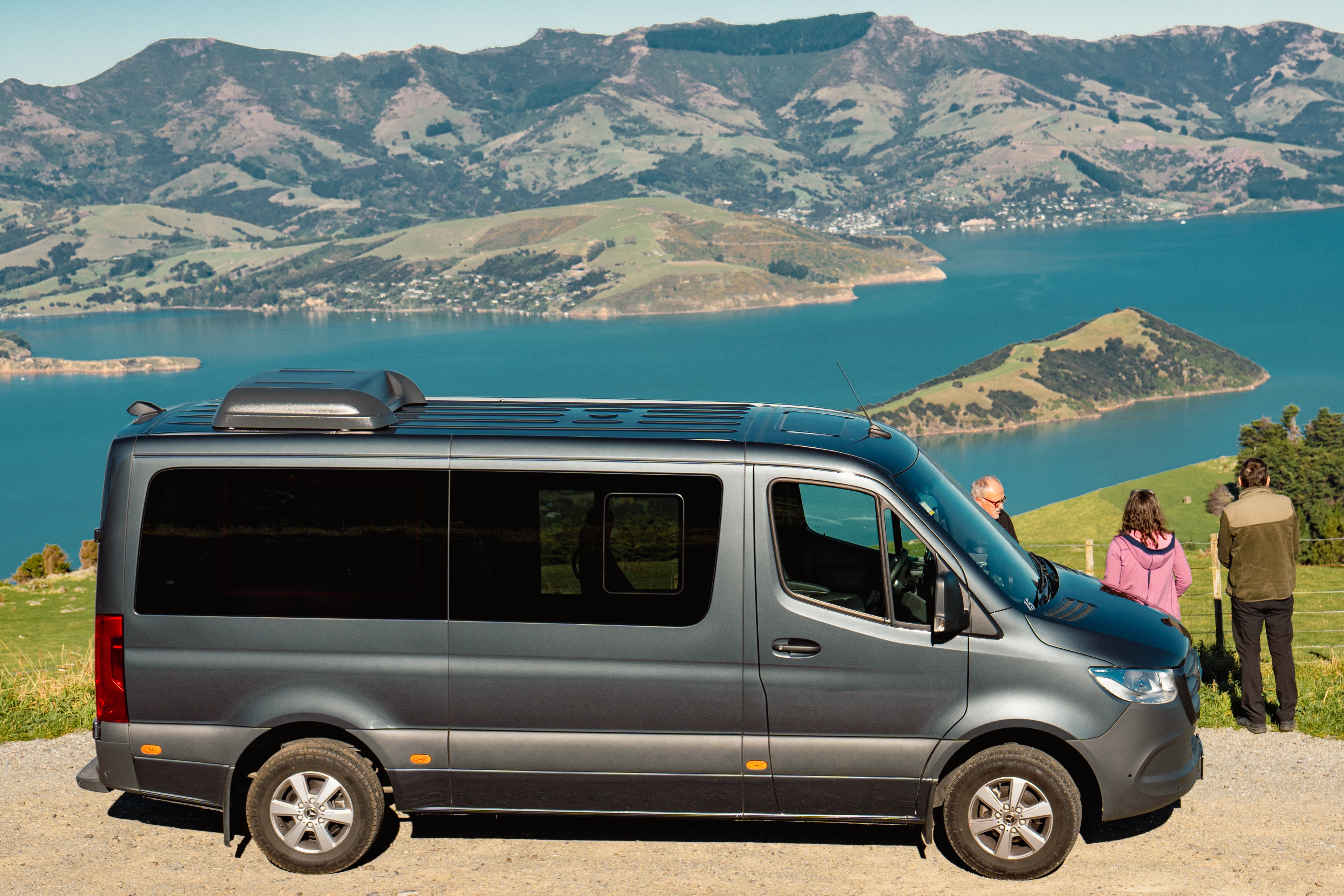 Guests beside a Canterbury Trails Mercedes-Benz Sprinter at a lookout above Akaroa Harbour
