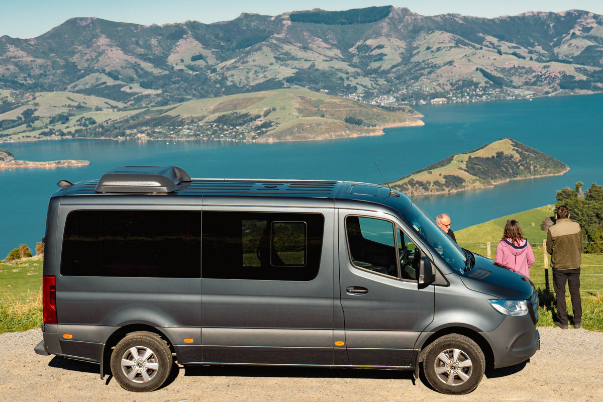 Guests beside a Canterbury Trails Mercedes-Benz Sprinter at a lookout above Akaroa Harbour