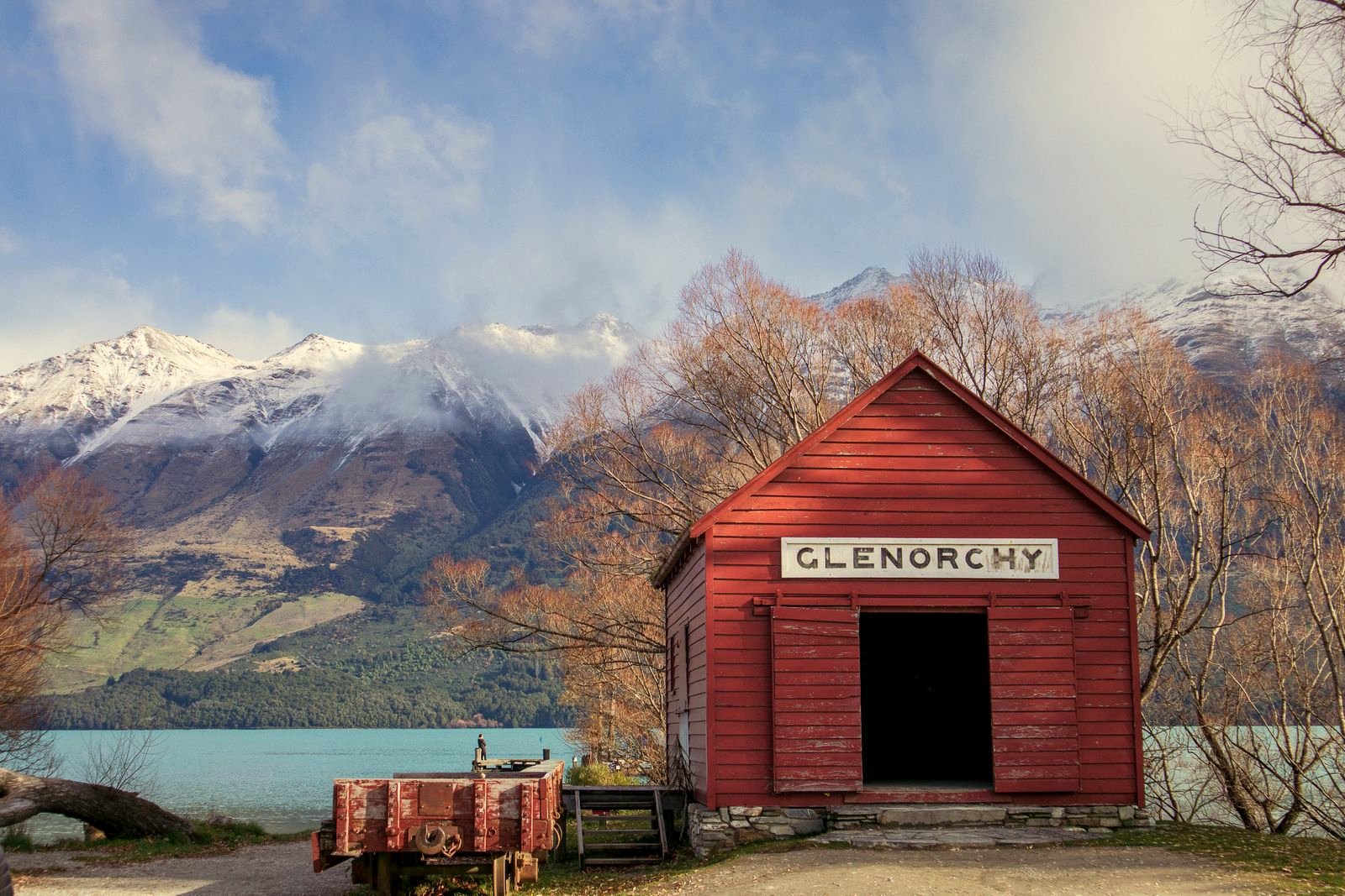 The historic red Glenorchy shed beside Lake Wakatipu with snow capped mountains beyond