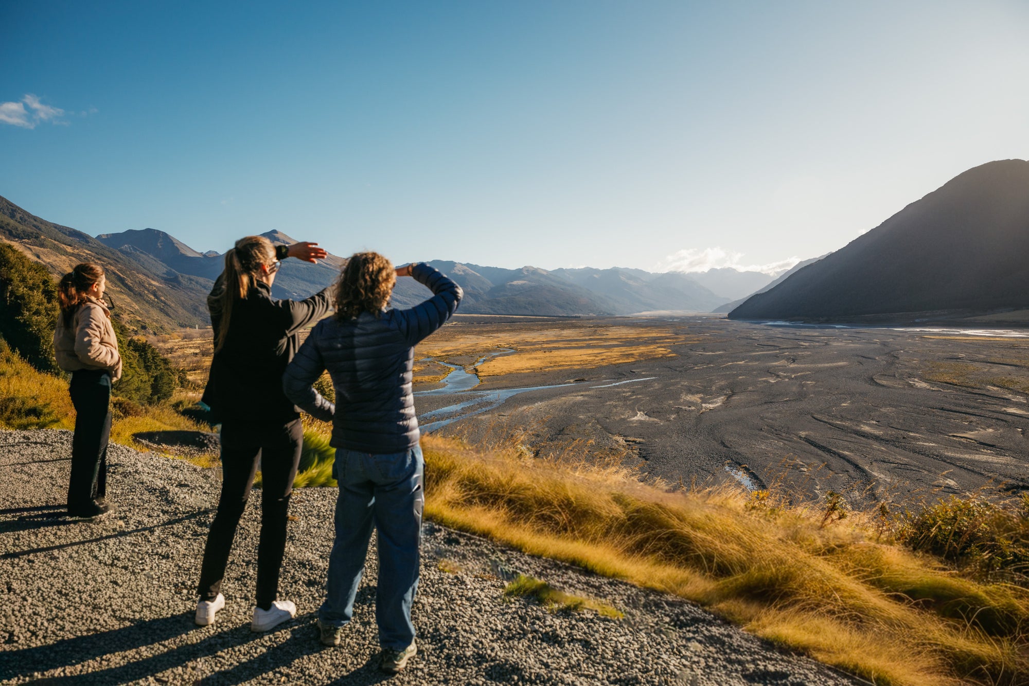 Luxury tour of South Island New Zealand. Three people standing on a gravel path overlooking a valley with mountains in the background.