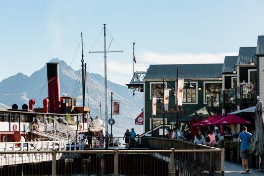 A view of Queenstown's waterfront with a mountain in the background, featuring a clear blue sky.