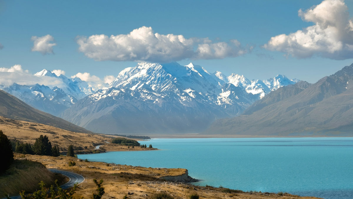 Aoraki Mount Cook above the turquoise water of Lake Pukaki, with tussock and an empty road below