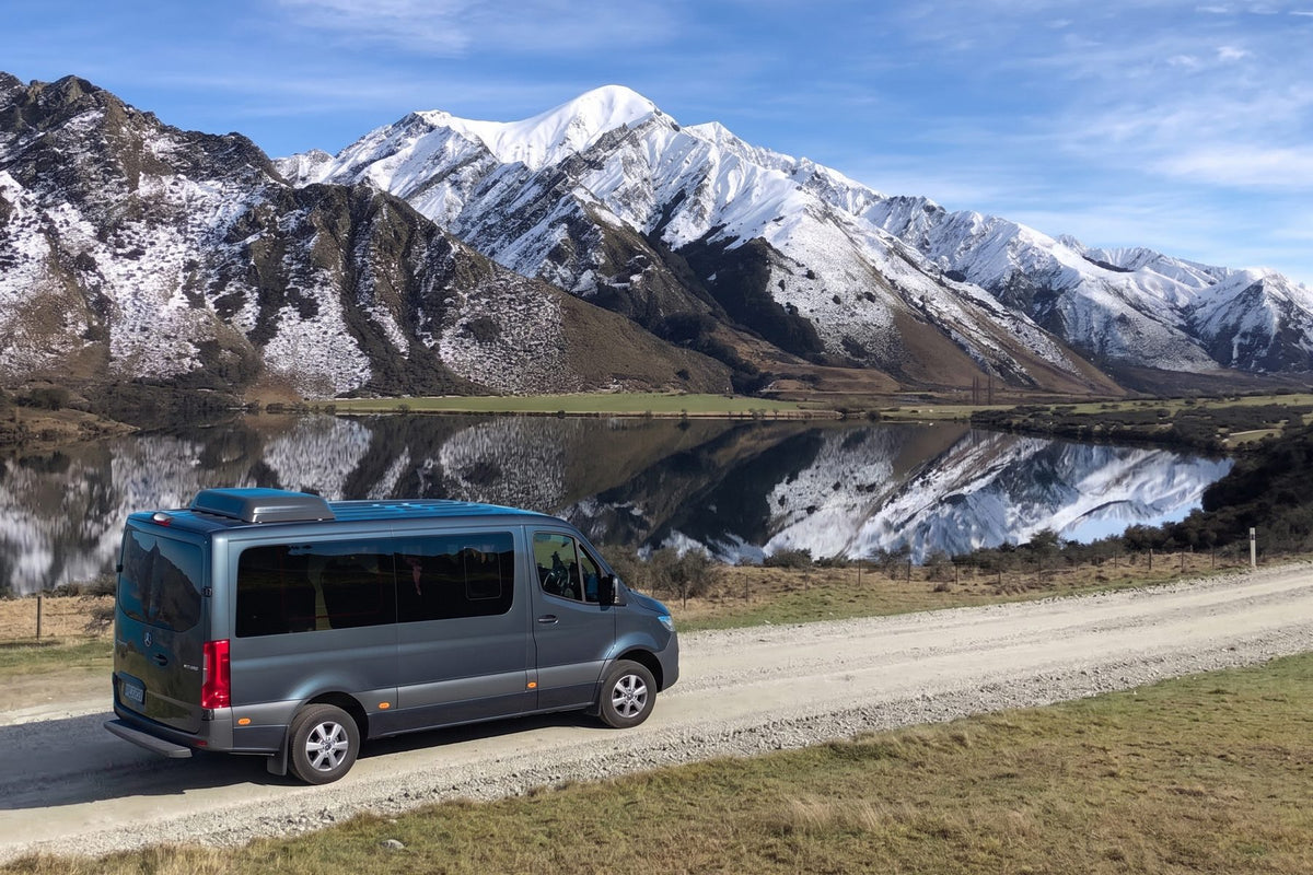 A private Mercedes-Benz vehicle beside Moke Lake, with snow-capped peaks reflected in the water