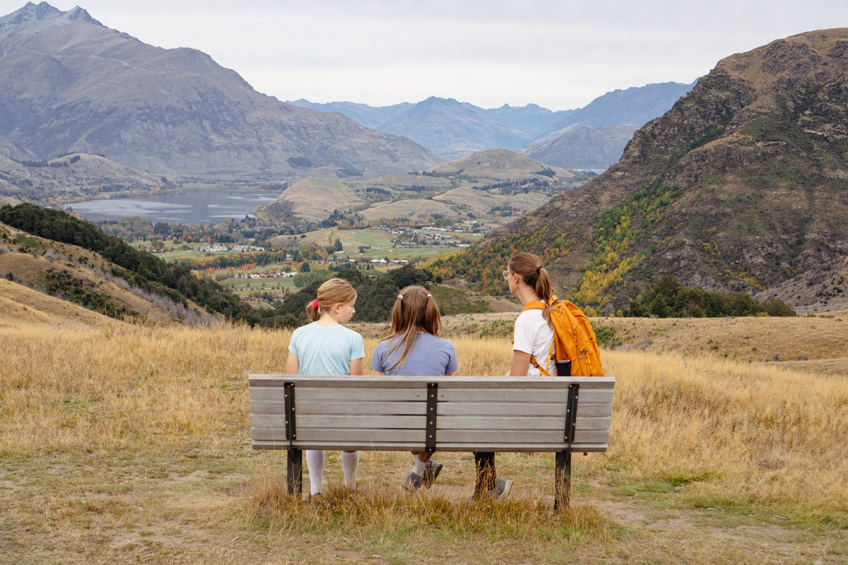 Three walkers on a bench above Arrowtown, looking out over Lake Hayes and the Wakatipu Basin